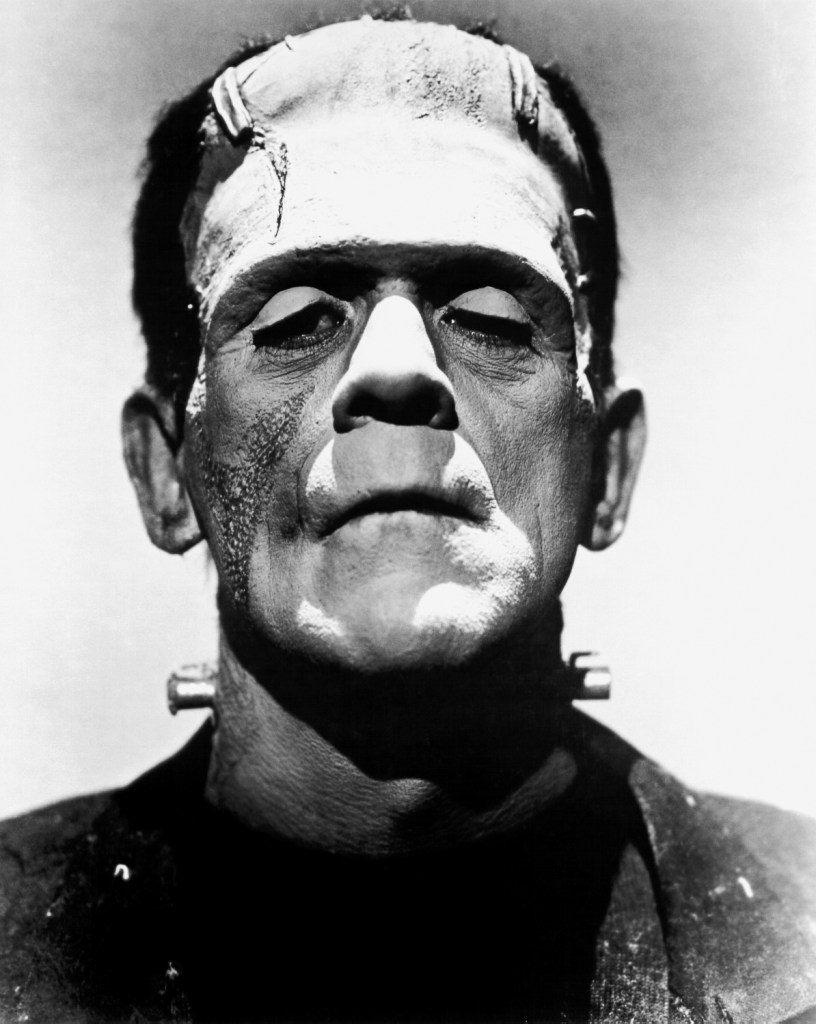 A black-and-white close-up of Frankenstein’s monster with his eyes half closed. His broad forehead bears scars and stitches, metal bolts protrude from his neck, and his heavy features appear somber and lifeless. The lighting highlights the rough texture of his skin and the square shape of his head, emphasizing his tragic, constructed nature.