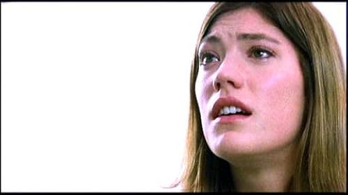 Close-up film still of a young woman looking upward with a fearful, anguished expression. Her face is softly lit against a stark white background, highlighting her wide eyes and parted lips as if she is on the verge of speaking or crying out.