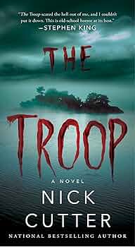 Book cover for The Troop by Nick Cutter. The cover shows a small, dark island surrounded by water under a foggy green-blue sky. The title ‘The Troop’ appears in large red letters that resemble dripping blood. The author’s name, Nick Cutter, appears below the title. The overall tone is ominous and horror-themed.
